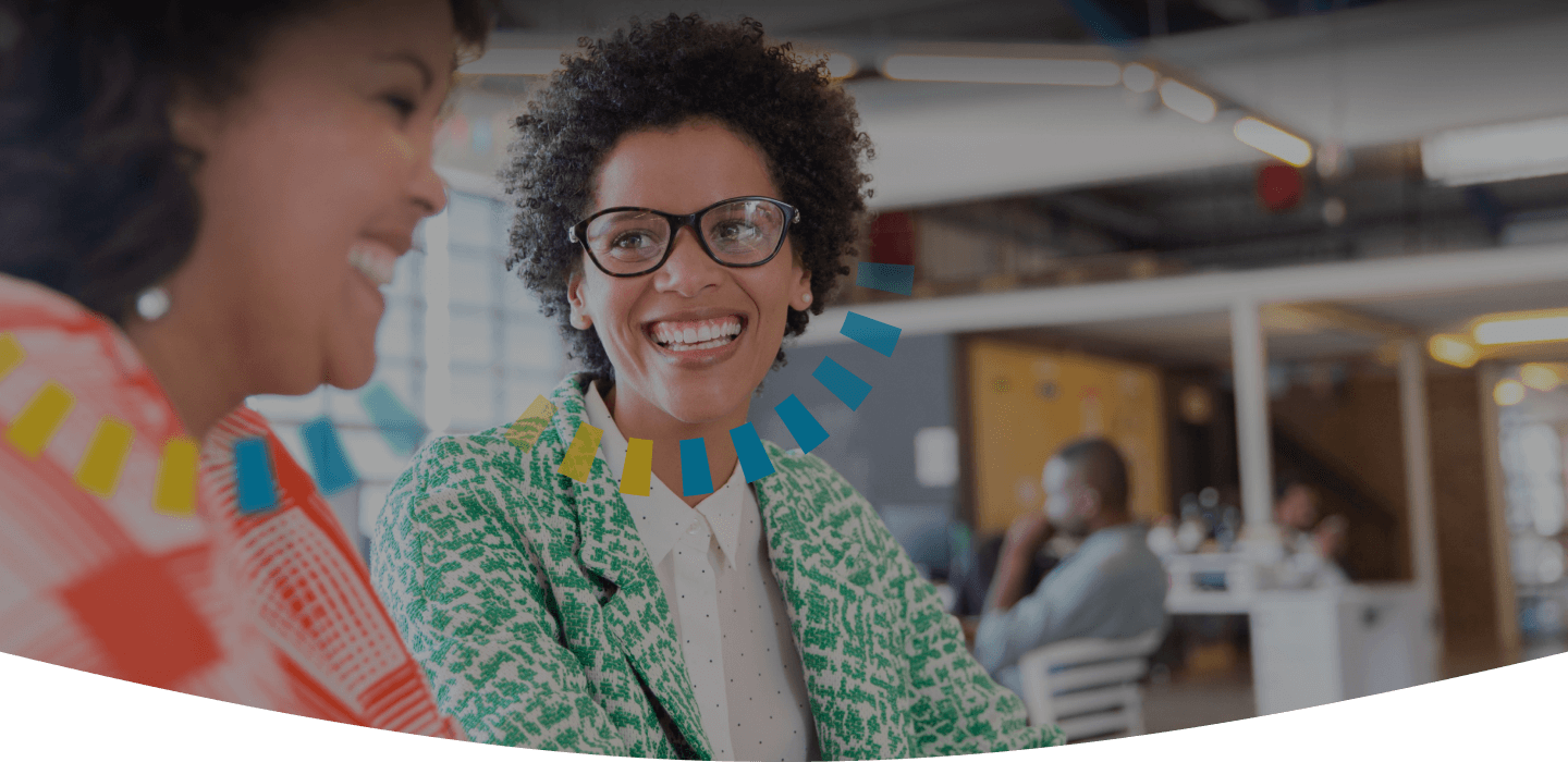 Two women smiling while working together in an office setting. One women has an SC DiSC style halo and the other has a CS DiSC style halo.