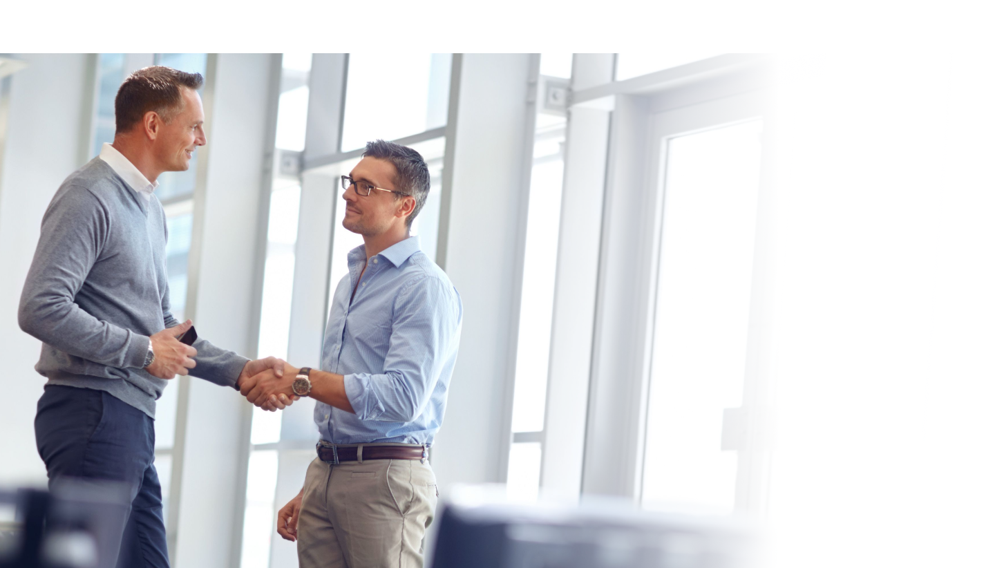 Two men shaking hands wearing semi casual business attire while in an office setting.