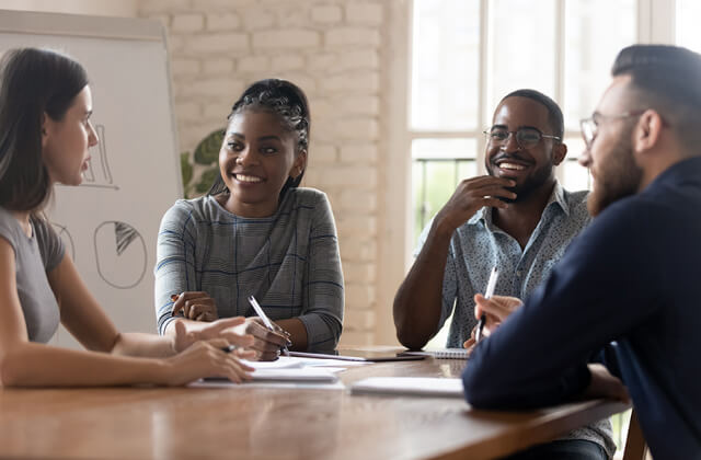 Group of smiling coworkers in a meeting sitting around a table. 