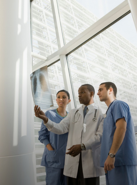 A group of three healthcare professionals reviewing an x-ray of lungs. 
