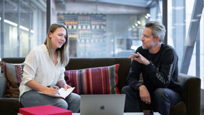 Two coworkers sitting on a couch discussing something on a laptop.
